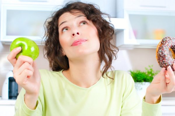 Diet. Beautiful Young Woman choosing between Fruits and Sweets