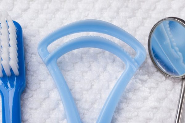 Oral hygiene health concept. Closeup dental tools blue toothbrush mirror and tongue cleaner on white towel