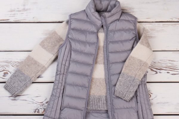 Combination of vest and sweater for chill autumn weather. New collection items on a wooden shelf.