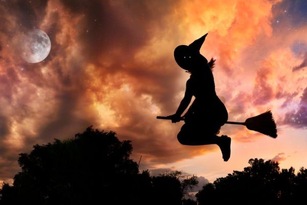 Halloween witch silhouette with glowing eyes flying on broomstick in the evening at dramatic sky with moon and stars