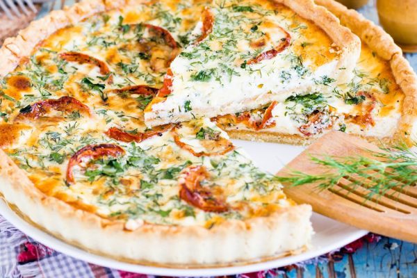 Sliced homemade french quiche pie with tomato, cheese and herb on a plate.