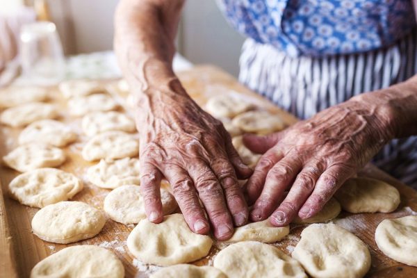 Senior woman baking pies in her home kitchen. Cutting out circles from raw dough.