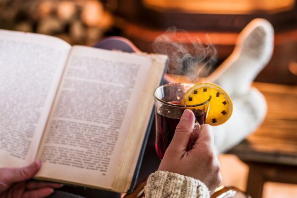 Hot mulled wine and book in woman hands. Relaxing in front of burning fire in the cold winter day.