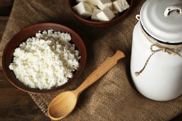 Milk can with cottage cheese on wooden background
