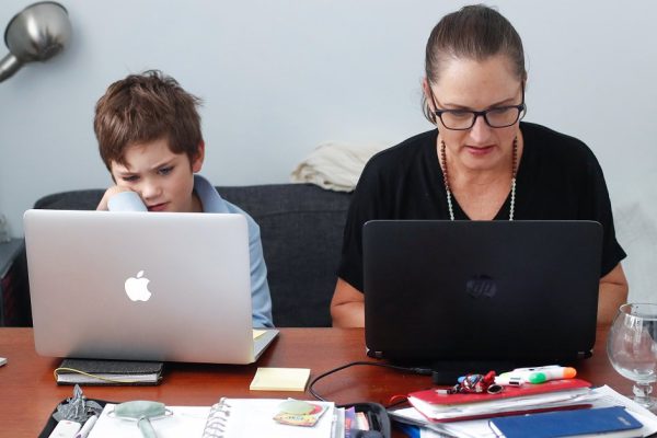 SYDNEY, AUSTRALIA - APRIL 09: Phoenix Crawford does school work on a laptop while his mum Donna Eddy replies to client emails on April 09, 2020 in Sydney, Australia. Massage therapist and acupuncturist Donna Eddy is able to continue running her business from home as a clinical practitioner after the Federal and State governments implemented tough restrictions and the closure of non-essential business due to COVID-19. While Donna has always maintained a strict cleaning regimen in her work space, it has now increased in response to the current coronavirus (COVID-19) pandemic with table linen changed, surfaces such as door handles wiped down and floors mopped between each patient who must wash or sanitize hands on arrival. A single mother to 8-year-old Phoenix, Donna Eddy is also juggling home schooling while running her business.  Phoenix, who is in Year Two at primary school, now has a routine where he can complete school work while his mother treats patients throughout the day, however Donna says it is still a struggle to balance her work and making sure she is available to help her son when he needs help with his online work. The Australian government introduced tough restrictions in response to the ongoing COVID-19 pandemic, closing non-essential businesses and imposing limits of peoples movement, gatherings and social distancing measures. Public gatherings are now limited to two people, while Australians must stay stay home unless absolutely necessary. New South Wales and Victoria have also enacted additional lockdown measures to allow police the power to fine people who breach the two-person outdoor gathering limit or leave their homes without a reasonable excuse. Queensland, Western Australia, South Australia, Tasmania and the Northern Territory have all closed their borders to non-essential travellers and international arrivals into Australia are being sent to mandatory quarantine in hotels for 14 days. (Photo by Brendon Thorne/Getty Images)