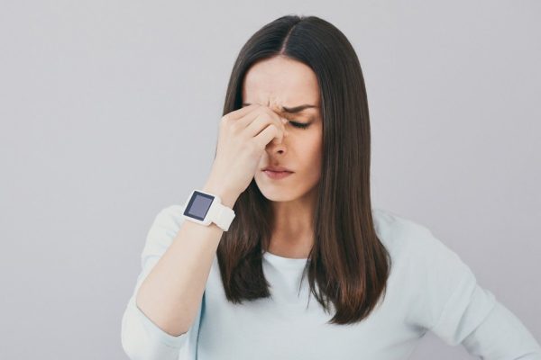 Sad days. Pretty brunette woman touching eyes and feelling tired while standing against isolated white background.
