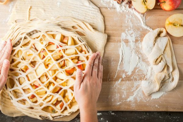 Cooking apple pie, kitchen wooden table, the girl (his hands in the frame) decorates the cake, top view