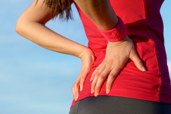 Female athlete lower back painful injury. Caucasian fitness girl gripping her lowerback because sport injury after exercising and running.