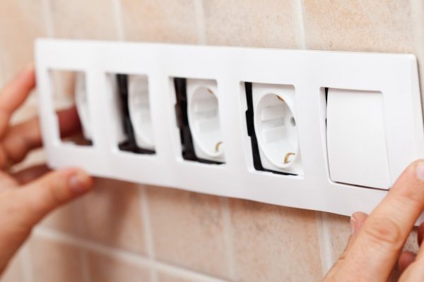 Hands installing decorative frame on electrical sockets in the wall - closeup