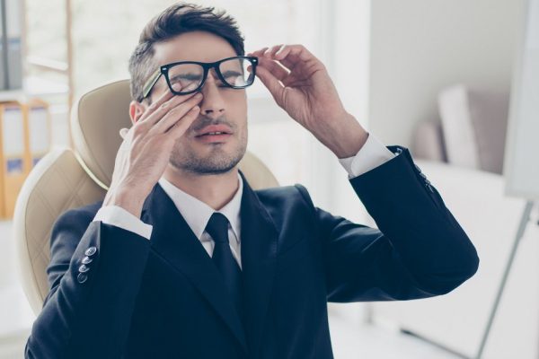 Health care healthcare people. Close up portrait of sad unhappy exhausted frustrated tired sleepy employee manager banker touching eyes holding glasses sitting at light modern office