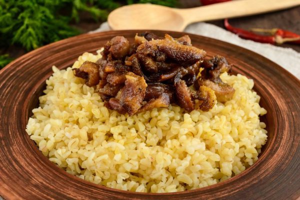 Eastern traditional wheat porridge - bulgur with roasted pieces fatty meats, bacon in a clay bowl on dark wooden background.