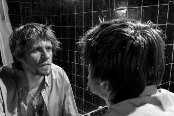 Drunk Man looks at himself in the mirror in a bathroom. grayscale image