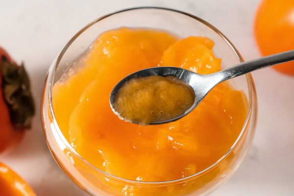 Glass and spoon with persimmon jam on table, top view