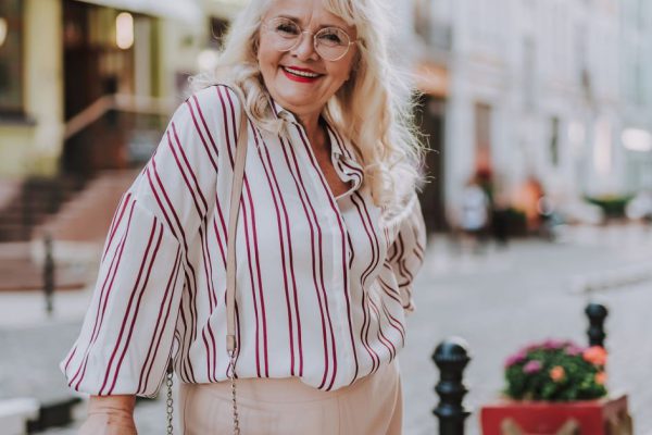 Waist up photo of beautiful female. White-haired lady dressed in striped blouse and beige pants