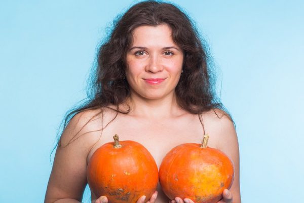 Young happy woman holds pumpkin in hands above her breast. Plastic surgery and silicone implants concept