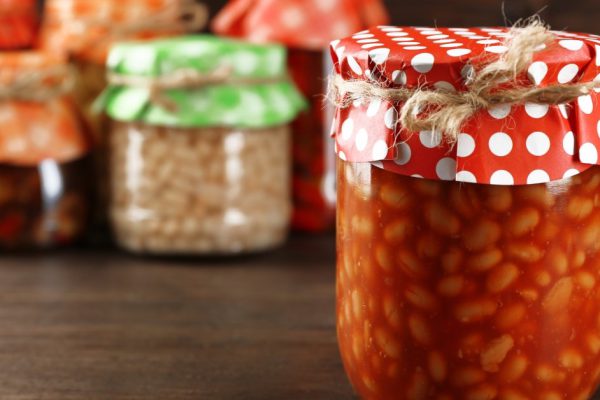 Jars with pickled vegetables and beans on wooden background