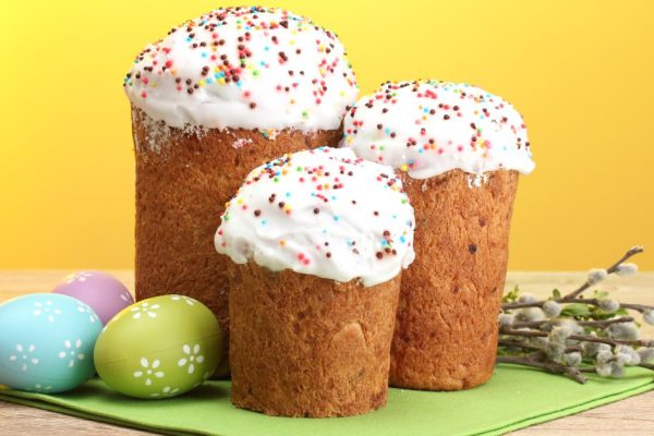 Beautiful Easter cakes, colorful eggs and pussy-willow twigs on wooden table on yellow background