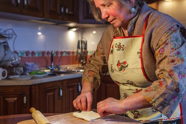 An elderly woman in an apron prepares pies in the kitchen