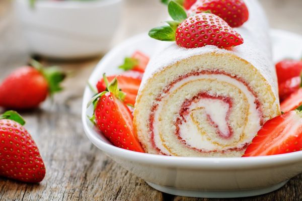 cake roll with strawberries and cream cheese on a dark wood background. tinting. selective focus