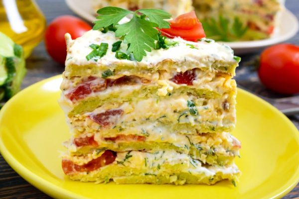 A piece of delicious cake of zucchini, tomatoes and cheese on a wooden table. Vegetable cake.