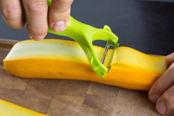 Man making slices of zucchini with vegetable peeler for a beautiful dish