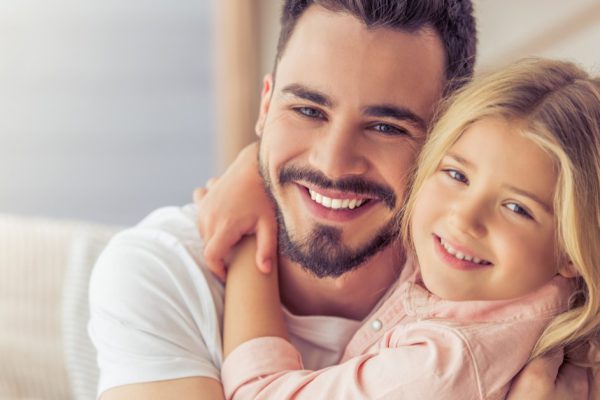 Portrait of handsome father and his cute daughter hugging, looking at camera and smiling
