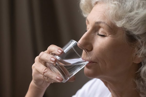 Thirsty elderly woman drink clear pure mineral water from glass, take daily dose for body balance and refreshment, mature female enjoy clean still aqua, hydration, healthy lifestyle concept