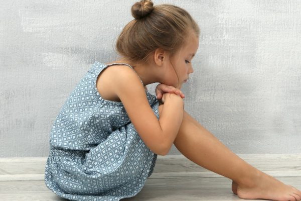 Sad little girl sitting on floor in empty room
