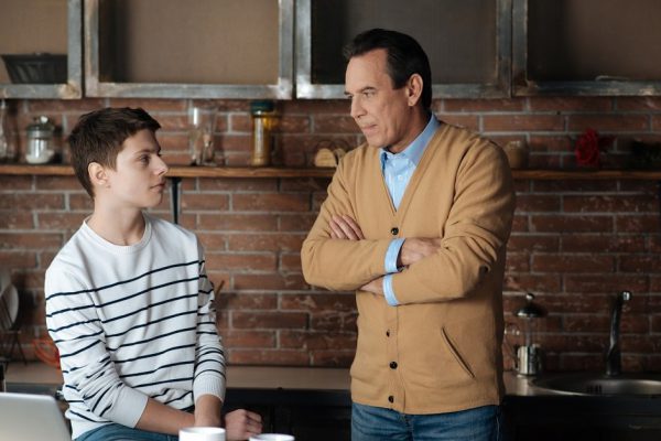 Look at me. Strict man pressing lips crossing arms on chest while standing opposite his child