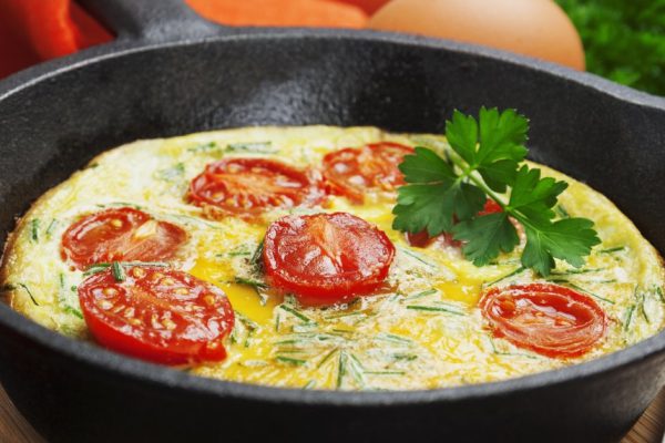Scrambled Fried eggs with tomatoes in a cast iron pan on the table