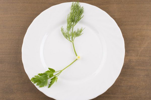plate with green grass with dill and  fennel  in the form of dial,  on white brown wooden texuted table