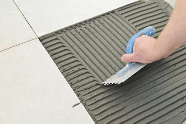 Laying Ceramic Tiles. Troweling mortar onto a concrete floor in preparation for laying white floor tile.