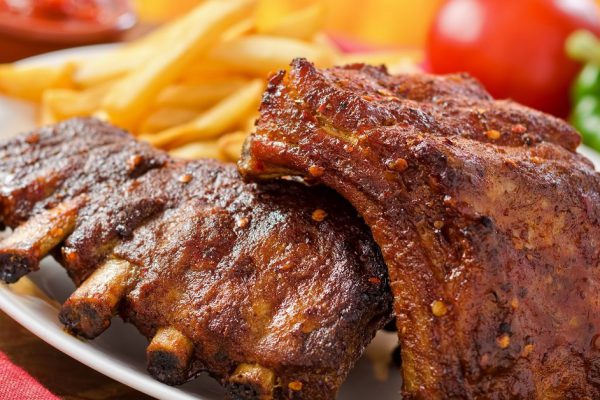 Barbecued pork baby back ribs against a hardwood fire background.