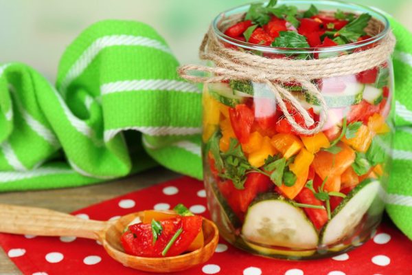 Vegetable salad in glass jar on wooden table, on bright background