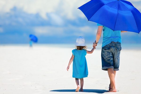Father and daughter at beach with umbrella to hide from sun