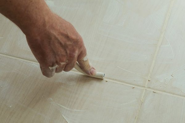 Workers hand smoothing the grout  joints between tiles using a rubber stick