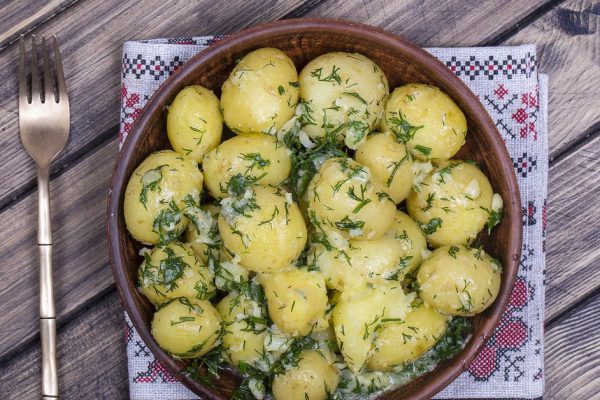 Boiled young potatoes with dill, garlic and butter in a plate on wooden table, close up