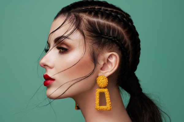 Brunette girl with perfect makeup. Beautiful model woman with curly hairstyle. Care and beauty hair products. Lady with braided hair. Model with jewelry. Turquoise background