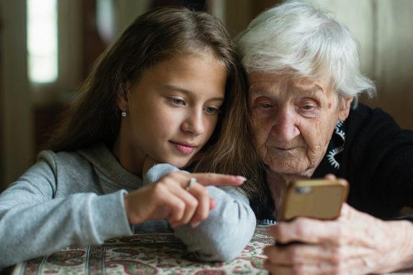 A little cute girl teaches her grandmother to use a smartphone.
