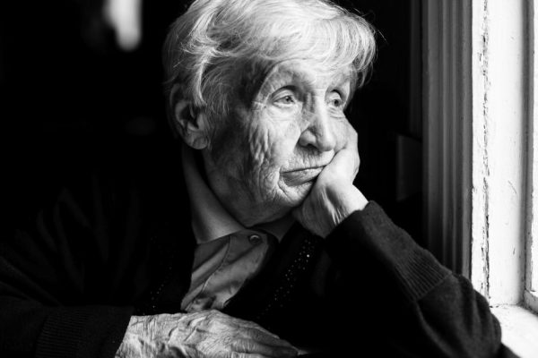 Elderly woman sadly looking out the window, a black-and-white photo.