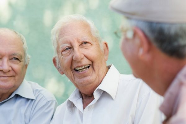 Active retirement, group of three old male friends talking and laughing on bench in public park