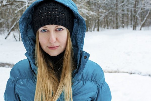 Portrait of a beautiful young woman in a turquoise feather bed and a knitted cap on a background of a winter park